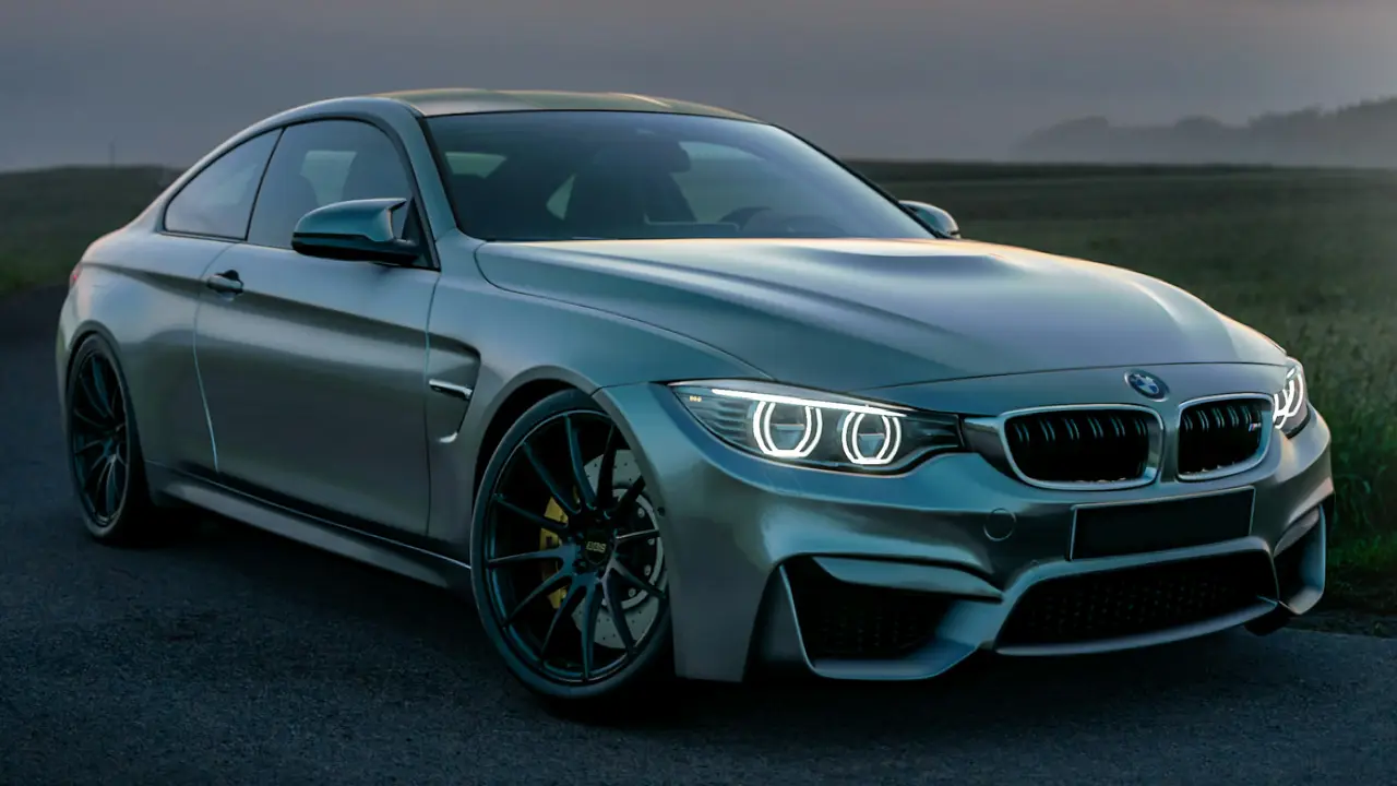 Close-up of glowing angel-eye headlights on a grey BMW M4 at dusk